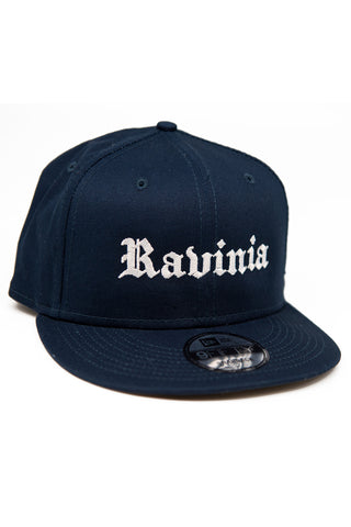 A navy blue baseball cap with Ravinia in white in Gothic script, and a New Era sticker on the bill.