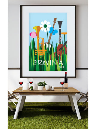 A framed Ravinia poster featuring instruments in grass, surrounded by butterflies and flowers, with a table with wine glasses and a wine bottle on it below.