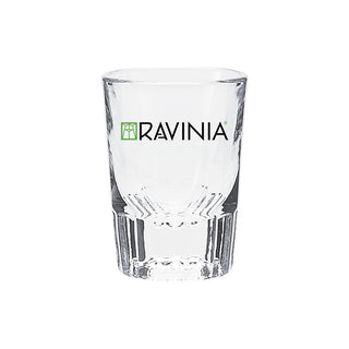 A clear, empty shot glass with the Ravinia logo on it.