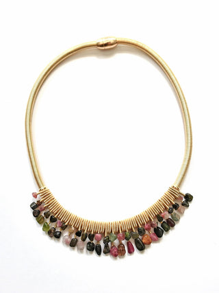 A necklace made of thick, gold-toned piano wire with two tiers of varied-colored stones hanging from it.