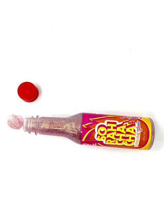 An overhead view of an open bottle that looks like hot sauce, with red glitter inside and a label that reads, So Rah Cha Cha. Glitter is visible to the left of the bottle.