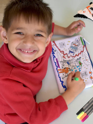 A boy looking up, smiling, as he colors in the space-themed pencil case.