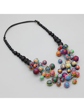 An angled view of a necklace with five stately strands of multi-colored beads covered in threads are delicately hanging from a row of black beads.