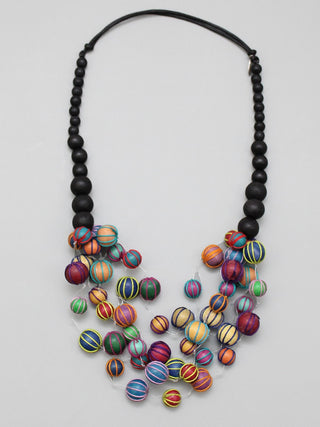 An overhead view of a necklace with five stately strands of multi-colored beads covered in threads are delicately hanging from a row of black beads. 