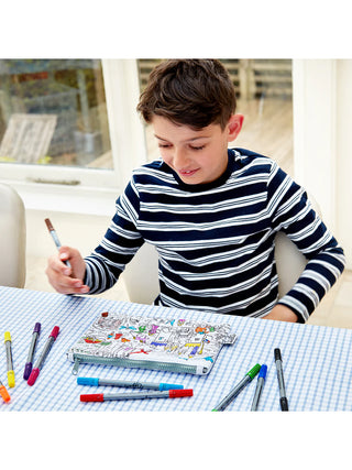 A smiling boy coloring on the fairy tale pencil case with colored markers.
