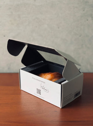 The Real Bread Lamp packaging includes a clear panel in its top and the designer’s signature on its side.