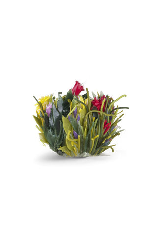 A vase that looks like it's made by nature, with red and purple flowers popping up among what appear to be green grasses and plants.