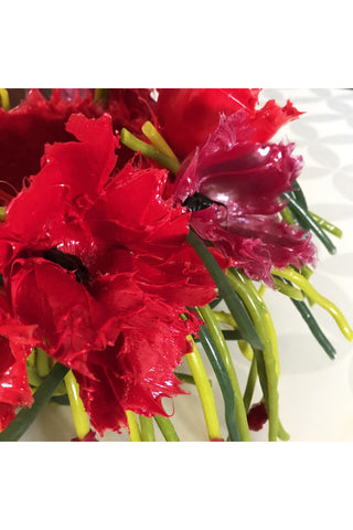 A close-up of red silicone poppies and faux grass that make up the vase.