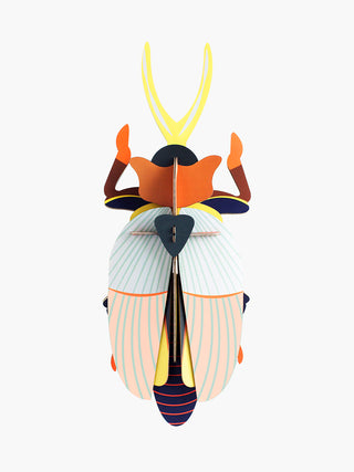 A large cardboard beetle with a blue and red body, orange head covering and yellow antenna.
