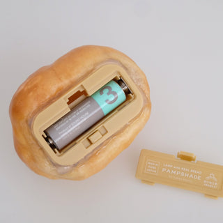 The back of the Petite Roll Real Bread Lamp shows its battery compartment door open, revealing the battery that powers it.